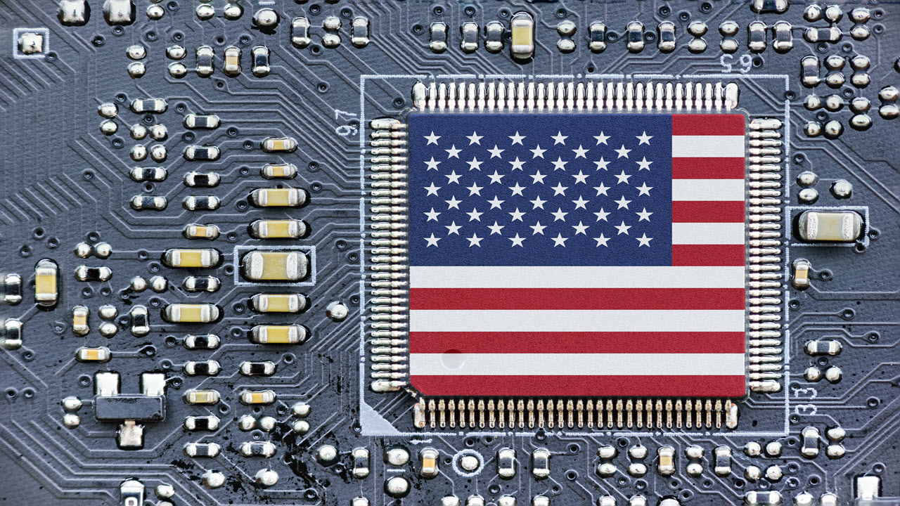 Symbolic American flag microchip on a dark printed circuit board with visible electronic components and circuit traces.